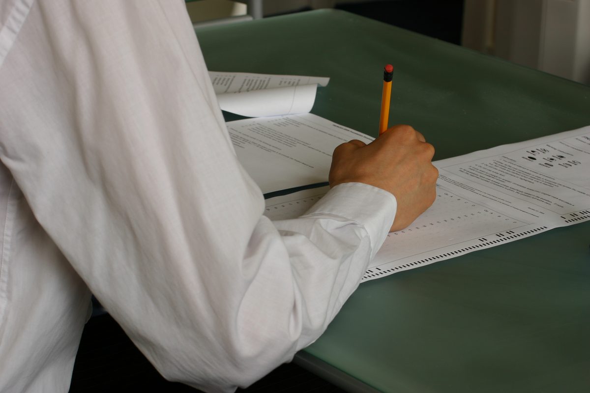 Élève qui remplit au crayon la copie d’un contrôle, sur une table de classe