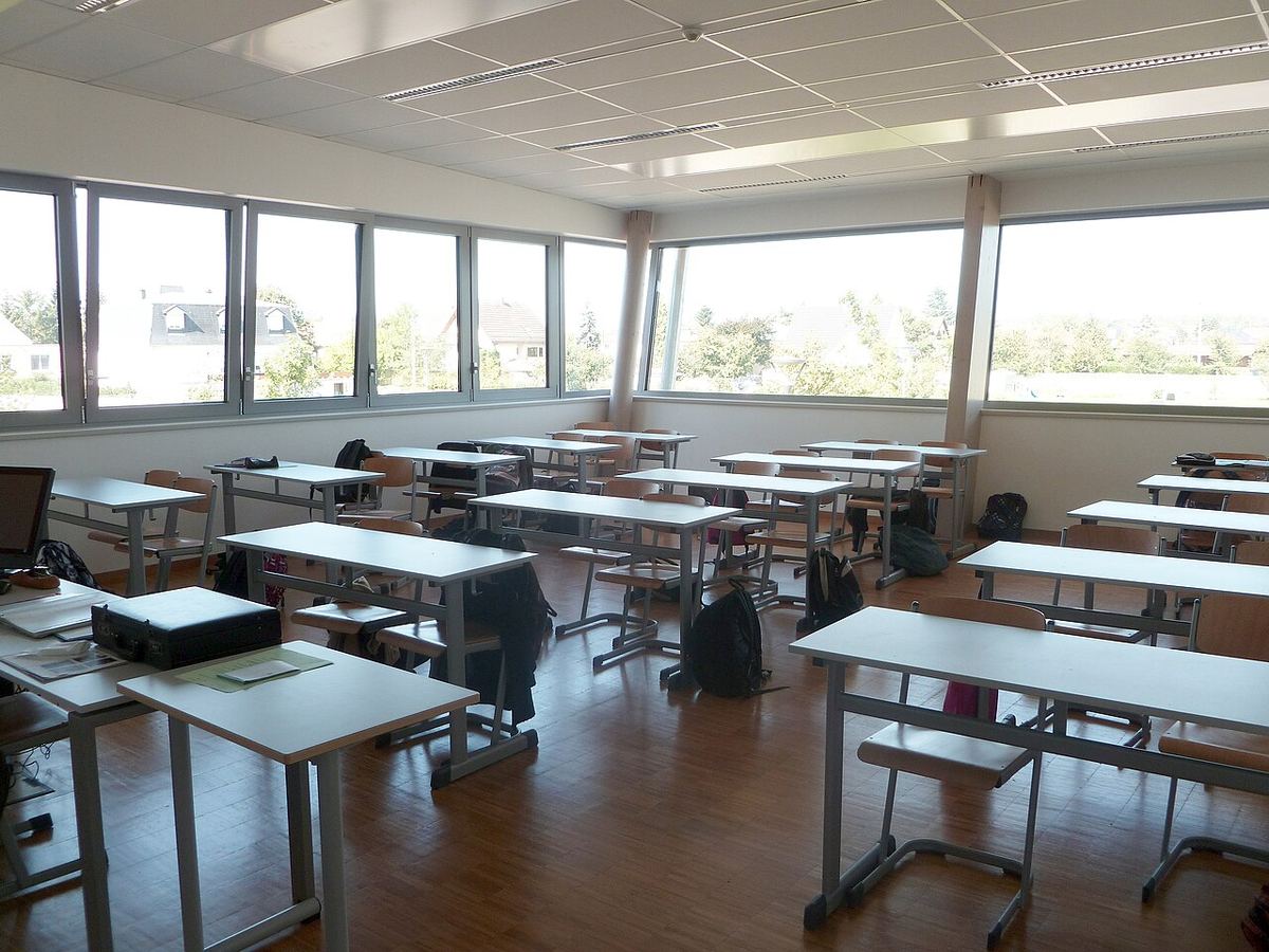 Salle de classe vide d’un lycée, tables et chaises en rangs, sacs et vestes posés sur les chaises