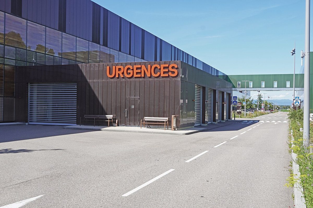 Enseigne orange « URGENCES » sur la façade d’un hôpital, au bord d’une route vide